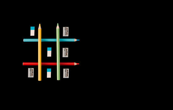 Game Iks Oks, wooden colored pencils, cutter, eraser. , concept of going to school, on black background