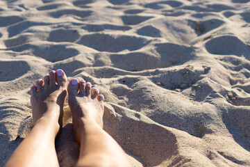 Close-up of legs and feet in the sand on the beach, with painted nails and tanned legs with copy space.