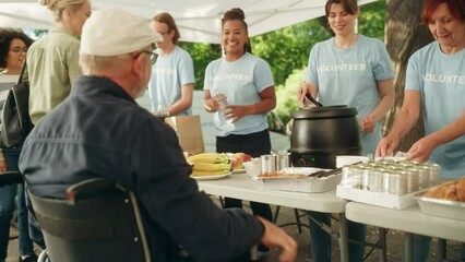 Group of Volunteers Helping in a Local Community Food Bank, Handing Out Free Food to People in Need in a Park on a Sunny Day. Man with Disabilities Using Wheelchair is Thankful for Charity Meal.