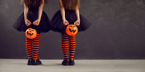 Copyspace background with children dressed in festive costumes for Halloween trick or treating. Two kids in orange black striped stockings holding pumpkin baskets, back view low section studio shot - Powered by Adobe