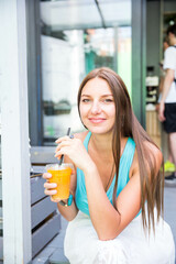 Authentic close up shot of an young brunette long hair woman drinking healthy dietetic biological natural orange juice from a transparent glass