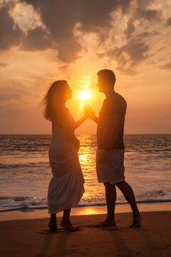 Silhouette lovely couple holding hands on tropical sandy beach at sea sunset background. Happy man and woman looking happiness. Joyful couple enjoying summer at ocean coastline. Copy text space