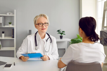 Portrait of professional friendly senior female doctor conducting consultation for patient. Mature...