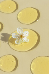 Drops of transparent cosmetic gel or serum yellow with a white flower on a beige background. The...