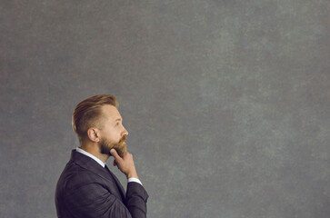 Thinking puzzled confused uncertain businessman looking forward at grey studio copy space. Side...