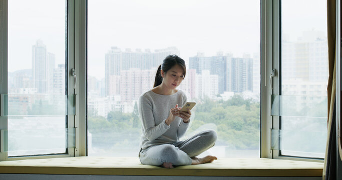 Woman use mobile phone and sit beside the window