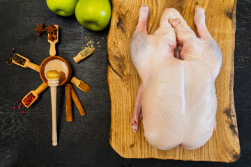 Raw whole duck, five spices: fennel, cloves, cinnamon, Sichuan pink pepper, star anise and honey. Green apples. Black background. Top view. Space for text. Everything you need to make Peking Duck.