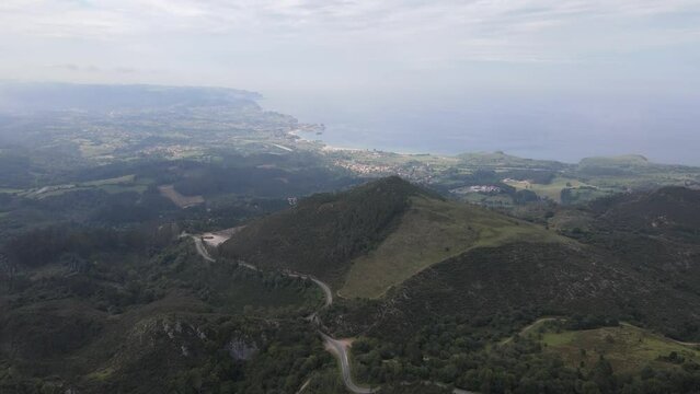 Misty drone flight over cooling green valleys and ocean in the distance.