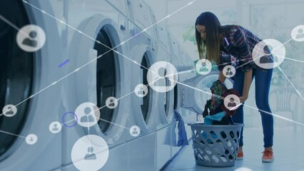 Video of biracial young woman putting clothes in washing machine with eye and networking icons - Powered by Adobe