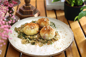 Potato dumplings, Polish knedle filled with fruit, served on a young cabbage, on a modern plate, on a wooden table.