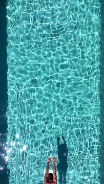 Vertical aerial top view of a man diving into fresh swimming pool water, background of a summer concept