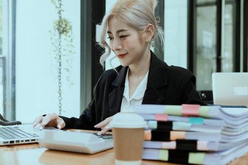 Happy smiling business woman Working on laptop computer with paperwork at desk in a modern office,  business finance technology concept.
