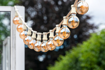 Light garland on the street at daylight. Decoration of the street with vintage Edison bulbs...