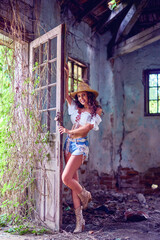 A beautiful brunette woman with long hair poses in the ruins of an old house.