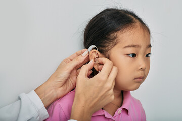 Asian little girl while installing BTE hearing aid by audiologist, close-up. Hearing solutions for...