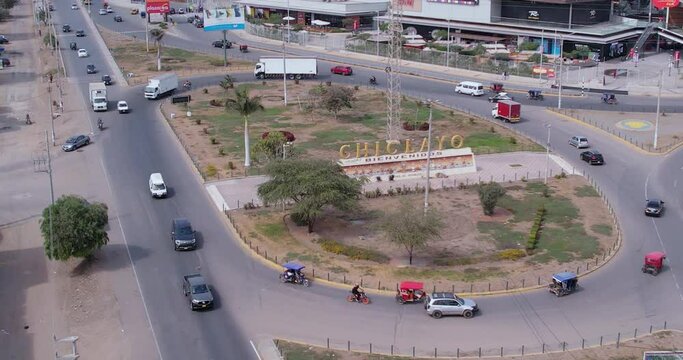 Beautiful drone shot of an oval on a Peruvian highway with passing cars around. Zoom in on a sign at the entrance to the city of Chiclayo in Peru in the morning.