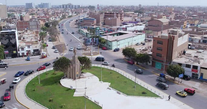 Amazing drone shot over the famous "Ovalo Quiñones" oval with a statue on the highway of the city of Chiclayo, Peru while cars drive around during the day.