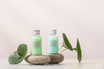 Obraz na płótnie Canvas Two transparent bottles with empty labels on podium of sea pebbles and water drops. Natural skin care cosmetic. Eco Beauty concept. Minimal composition