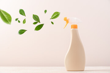 Spray bottle with cleaning product on light background with flying green leaves. Creative eco cleaning concept. Environmentally friendly home and office cleaning