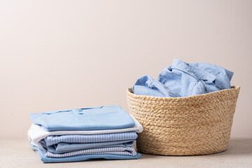 Stack of shirts and wicker basket with clothes on beige background. Laundry and dry cleaning service concept