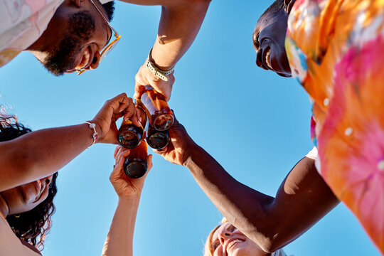 Happy multiethnic friends clinking beer bottles during summer party