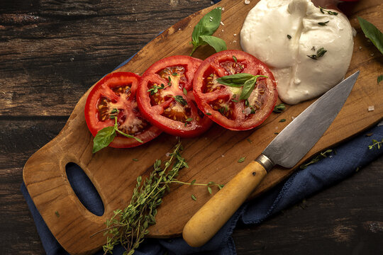 Appetizing fresh tomato and mozzarella cheese with herbs on wooden board
