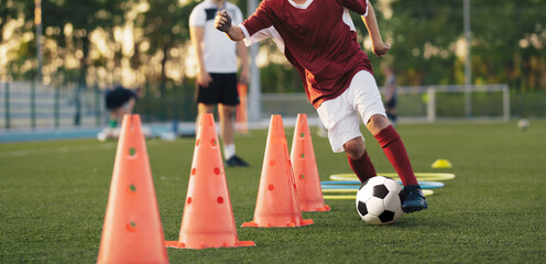 School boy running fast and kicking soccer ball on training slalom drill. Boy improving football...