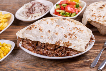 Meat doner kebab on the plate. Turkish meat doner kebab on wooden background. Served with hot lavash. Traditional Turkish cuisine. close up