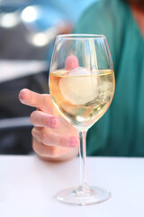 white wine glass with ice and human hand closeup photo on outdoor cafe background