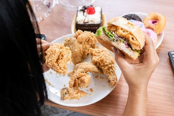 unhealthy woman eating fast food burgers, fried chicken, donuts and desserts, binge eating disorder concept