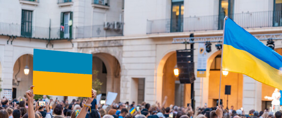 Manifestación con gente irreconocible, en una plaza contra la guerra, apoyando a Ucrania, con banderas y pancartas. Fotografía horizontal con espacio para texto. - obrazy, fototapety, plakaty