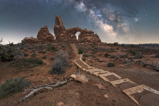 Steps leading to natural stone arch and canyon under starry sky with Milky Way