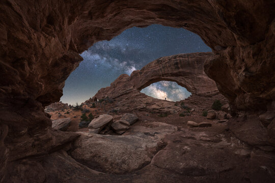 Anonymous traveler on natural rock arch under starry sky with Milky Way
