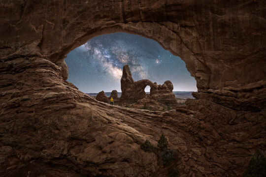 Anonymous person admiring stone arch and canyon under starry sky with Milky Way