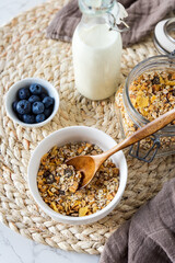 Knuspermüsli in einer Schüssel, Milch und frische Heidelbeeren auf einem Tisch. Nahaufnahme, gesundes Frühstück.