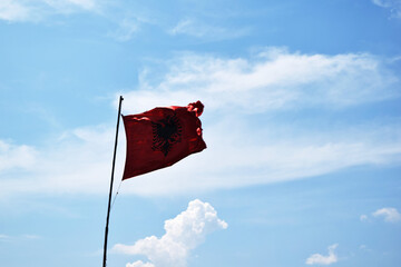 waving the flag of Albania against the blue sky