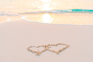 handwritten two heart on sand on Maldives island, concept of luxury travel and greetings for Valentine's Day
