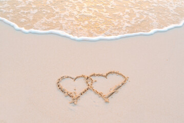 handwritten two heart on sand on Maldives island, concept of luxury travel and greetings for Valentine's Day