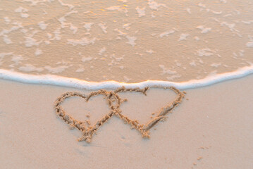 handwritten two heart on sand on Maldives island, concept of luxury travel and greetings for Valentine's Day