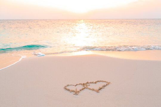 handwritten two heart on sand on Maldives island, concept of luxury travel and greetings for Valentine's Day