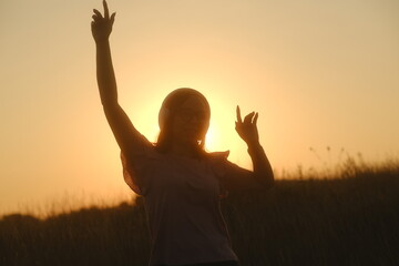 Beautiful woman in headphones and glasses dancing at sunset in the countryside at sunset in casual clothes