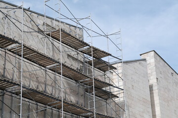 Facade restoration of building against cloudy sky. Reconstruction of building exterior with scaffolding.