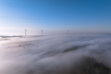 Aerial view of wind turbines rising above foggy landscape in sunny morning in Finland