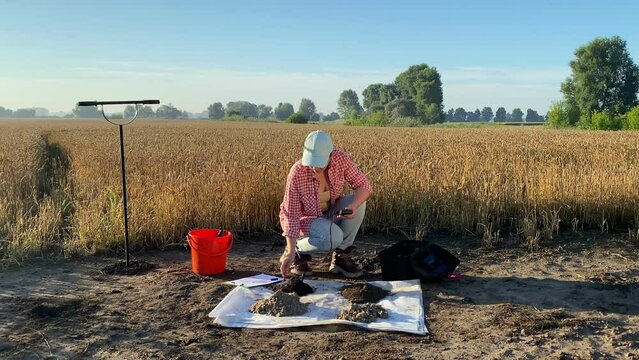 Female agronomist probing soil samples by using soil tester at sunrise outdoors. Woman agronomy specialist measuring pH value of soil by digital device at agricultural field. Environment research