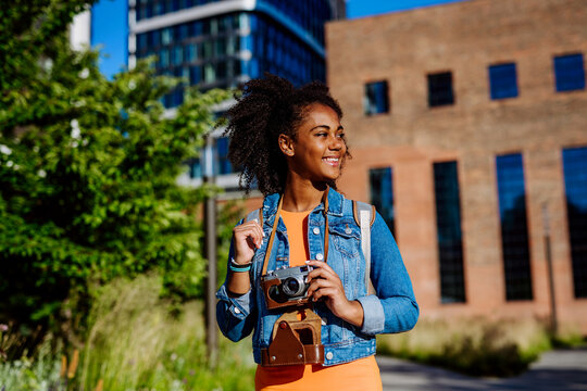Multiracial girl walking in city with camera, and taking photos.