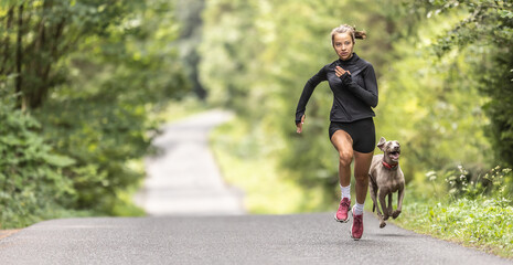 Female young sprinter runs fast up the hill followed by her dog