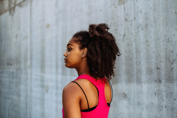 Rear view of young mulitiracial girl standing in front of city concrete wall.