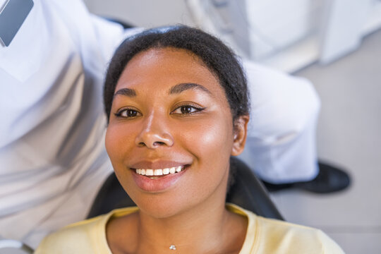 Woman laying at the dentist chair and smiling toothy while feeling satisfied after teeth whitening