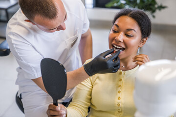 Male dentist helping put invisible braces aligner to the patient woman mouth