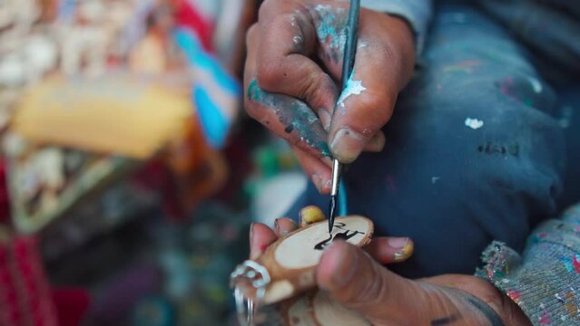 Close up shot of street painter hands painting wooden keychain on the street of Mall Road Manali, Himachal Pradesh, India. Urban lifestyle, street art concept.   street artist - painter